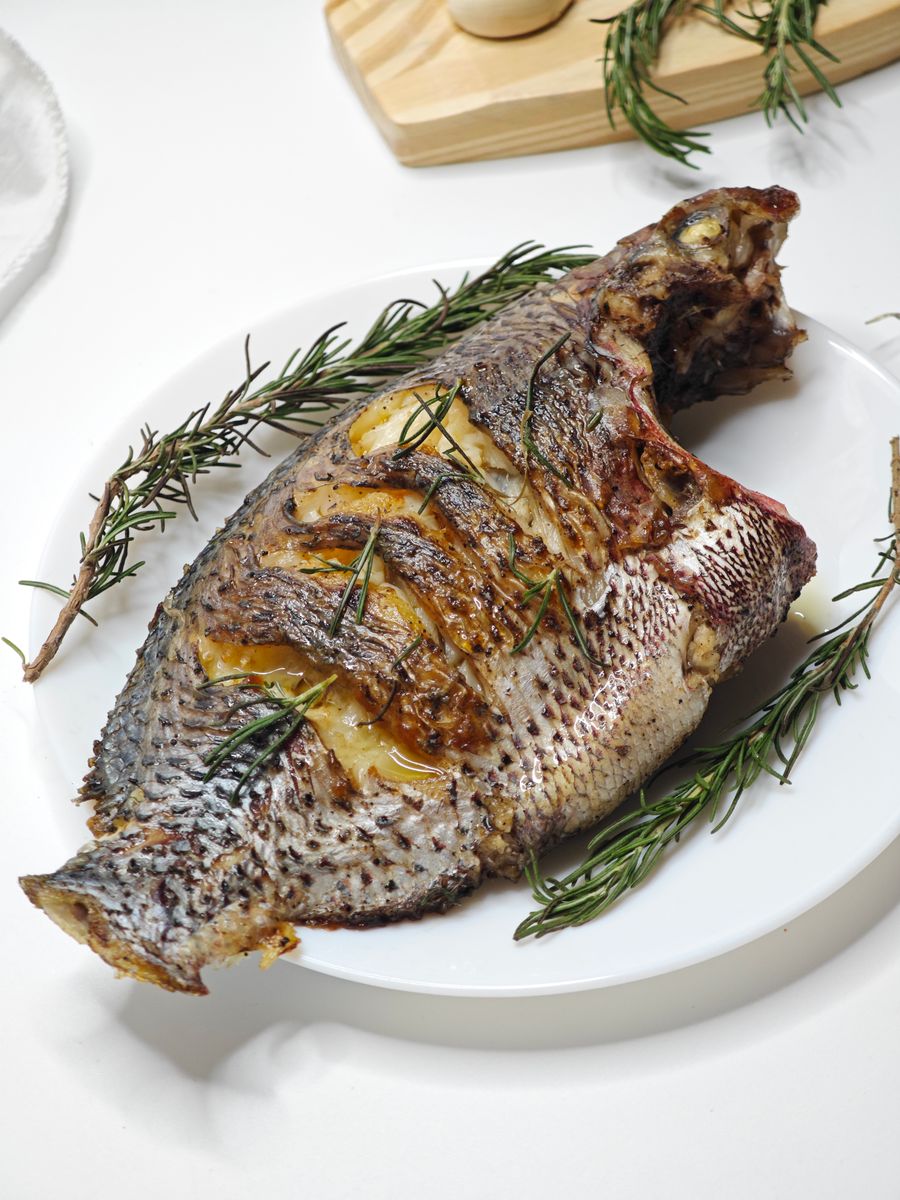 Ikan bakar dihidang dengan daun herba di atas pinggan putih